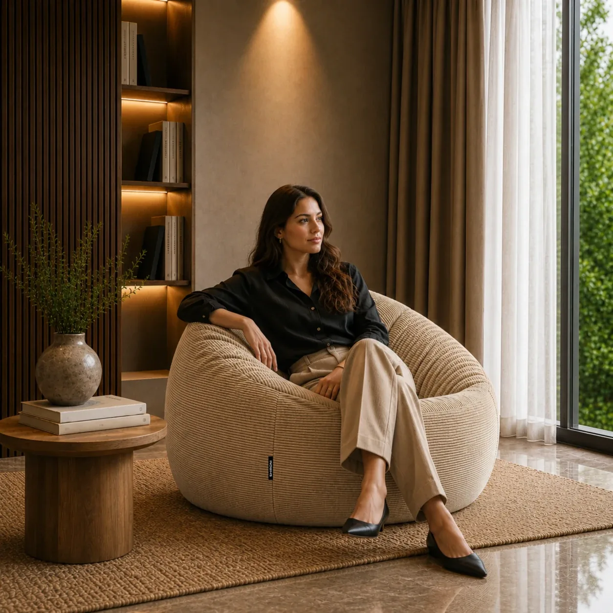Una persona sentada en el Puff SHIRONI IMOOSHI Beige, junto al ventanal de una sala